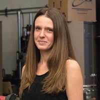 Sabbie Miller wearing a black sleeveless top poses in front of a production environment.