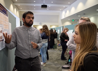 A person gestures at a poster presentation while explaining the research to someone else.