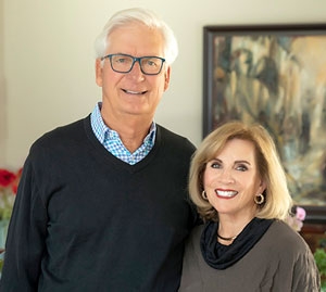 Donors Paul and Ruth Flowers pose in a living room in front of a wall with artwork.