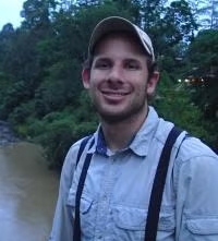 Headshot of Daniel Karp wearing a baseball hat in front of wetlands.